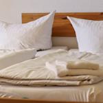 Zwei Betten mit weißen Kissen und Bettwäsche. Holzgestell und gefaltete Decke.