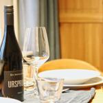 Tisch gedeckt mit Weinglas, Flasche und Geschirr. Holzmöbel und Tischtuch.