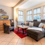 Wohnzimmer mit grauem Sofa, rotem Teppich und Holzmöbeln.