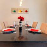 Esstisch mit sechs Stühlen, roten Servietten und einer Weinflasche.