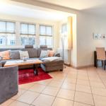 Wohn- und Essbereich mit Sofa, Tisch und Fenstern.