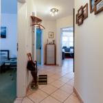 Flur mit Blick in Schlafzimmer und Wohnzimmer. Regal, Regenschirm und Bilder an der Wand.