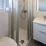 Badezimmer mit Dusche, Waschbecken und Toilette. Fenster mit Pflanze und Handtüchern.