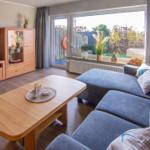 Wohnzimmer mit blauem Sofa, Holztisch und Blick auf Garten