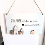 Hängendes Schild mit Text und Holzhäusern an Wand