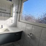 Badezimmer mit Waschbecken, Spiegel und getöntem Fenster