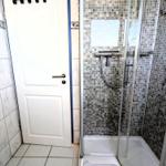 Bad mit Dusche und Fliesenwand. Tür und Bodenfliesen sind weiß.