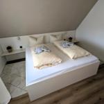 Schlafzimmer mit Doppelbett, Holzboden und Fenster. Weiße Wand und Bettgestell.