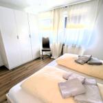 Schlafzimmer mit Doppelbett, weißen Schränken und Holzboden. Fenster mit weißen Vorhängen.