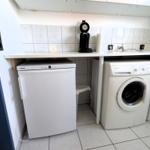 Waschmaschine, Trockner und Kühlschrank in einem hellen Raum mit Fliesenboden und Arbeitsplatte.