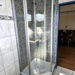 Dusche mit Glaswand und Mosaikfliesen, weiße Fliesen und Waschbecken sichtbar.