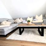 Ein Wohnzimmer mit grauem Sofa, Holztisch und Teppich auf Holzboden.