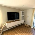 Wohnzimmer mit Fernseher, Holzboden und Terrassentür.