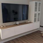 Wohnzimmer mit Fernseher, Schrank und Stehlampe auf Holzboden.