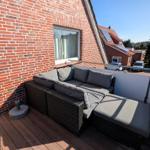 Terrasse mit Sitzgruppe, Holzboden und Blick auf Wohngebiet.