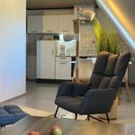Living room with armchair, coffee table, and kitchen in background.