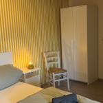 Bedroom with bed, nightstand, chair, and wardrobe against yellow-white striped wall.