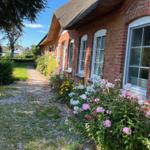 Red brick house with thatched roof and flower beds along a gravel path.