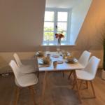 Dining room with table, four chairs, and window. Plant and flowers on the windowsill.