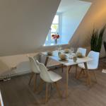 Dining table with four chairs under sloped ceiling with window and plant.