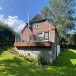 Haus mit Balkon, Grill und Garten. Hoher Dachfirst und roter Ziegelbau.