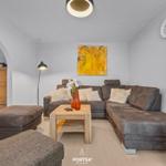 Wohnzimmer mit braunem Sofa, Holztisch und Wanduhr.