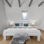 Schlafzimmer mit Dachschrägen, Bett, Nachttischen und Fenstern.
