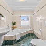Badezimmer mit Badewanne, Waschbecken und Toilette. Fenster mit Blick nach draußen.