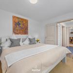 Schlafzimmer mit Bett, Nachttisch und Stuhl. Wandbild über dem Bett.