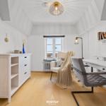 Schlafzimmer mit Schreibtisch, Sessel und Kleiderschrank. Holzboden und weiß gestrichene Wände.