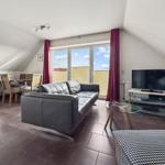Wohnung mit Sofa, Fernseher und Essbereich unter Dachschrägen.