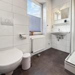 Badezimmer mit Toilette, Waschbecken und Dusche. Fenster mit Jalousie.