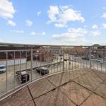 Terrasse mit Blick auf Straße und umliegende Gebäude unter blauem Himmel mit weißen Wolken.
