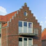 Rotes Ziegeldach und Backsteinfassade mit Balkon und runden Fenster.