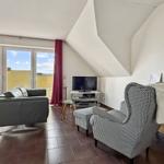 Wohnzimmer mit Sofa, Sessel und TV. Große Fenster und Dachschrägen.