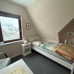 Schlafzimmer mit Dachschräge, Bett, Nachttisch und Fenster mit Blick auf Haus.