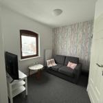 Ein Wohnzimmer mit Sofa, Fernseher und Fenster mit Blick auf die Straße.