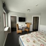 Schlafzimmer mit Bett, Fernseher und zwei Stühlen. Wandbild und Fenster sichtbar.