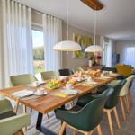 Esszimmer mit langem Tisch, Stühlen und Blick auf Garten.