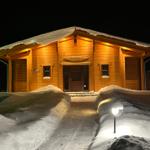 Holzhütte mit Schnee, beleuchteter Eingang und Weg