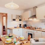 Küche mit Holzoberflächen, weißen Schränken und Küchenzeile. Esstisch mit Geschirr und Kaffeemaschine.