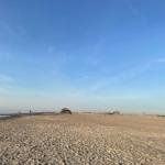 Weiterer Blick auf den Strand mit klarem Himmel und einigen Personen in der Ferne.