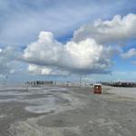 Strand mit Watt, Holzstegen und Strandkörben unter bewölktem Himmel