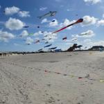 Strand mit vielen bunten Drachen im Himmel und Sandstrand im Vordergrund.