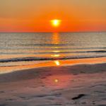 Sonnenuntergang über dem Meer mit Reflexion auf Sand und Wasser.