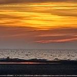 Sonnenuntergang über dem Meer mit goldenen Wolken und spiegelnder Wasseroberfläche.