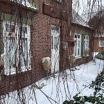 Rotes Backsteingebäude mit Schnee bedecktem Grundstück und weißen Fenstern.