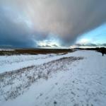 Schneebedeckter Weg durch eine offene Landschaft unter bewölktem Himmel.