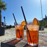 Zwei erfrischende Getränke mit Orangenscheiben stehen auf einem Holztisch am Strand.