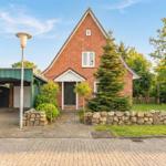 Rotes Backsteinhaus mit Vorgarten, Steinmauer und Carport.